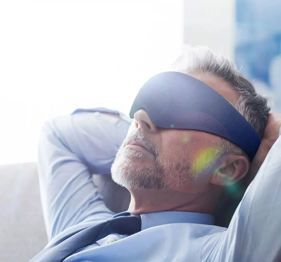 Man wearing a sleep mask with rainbow light effects, lying on a couch.